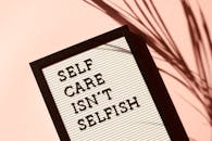 Letter board displaying 'Self Care Isn't Selfish' with artistic shadow on pink background.