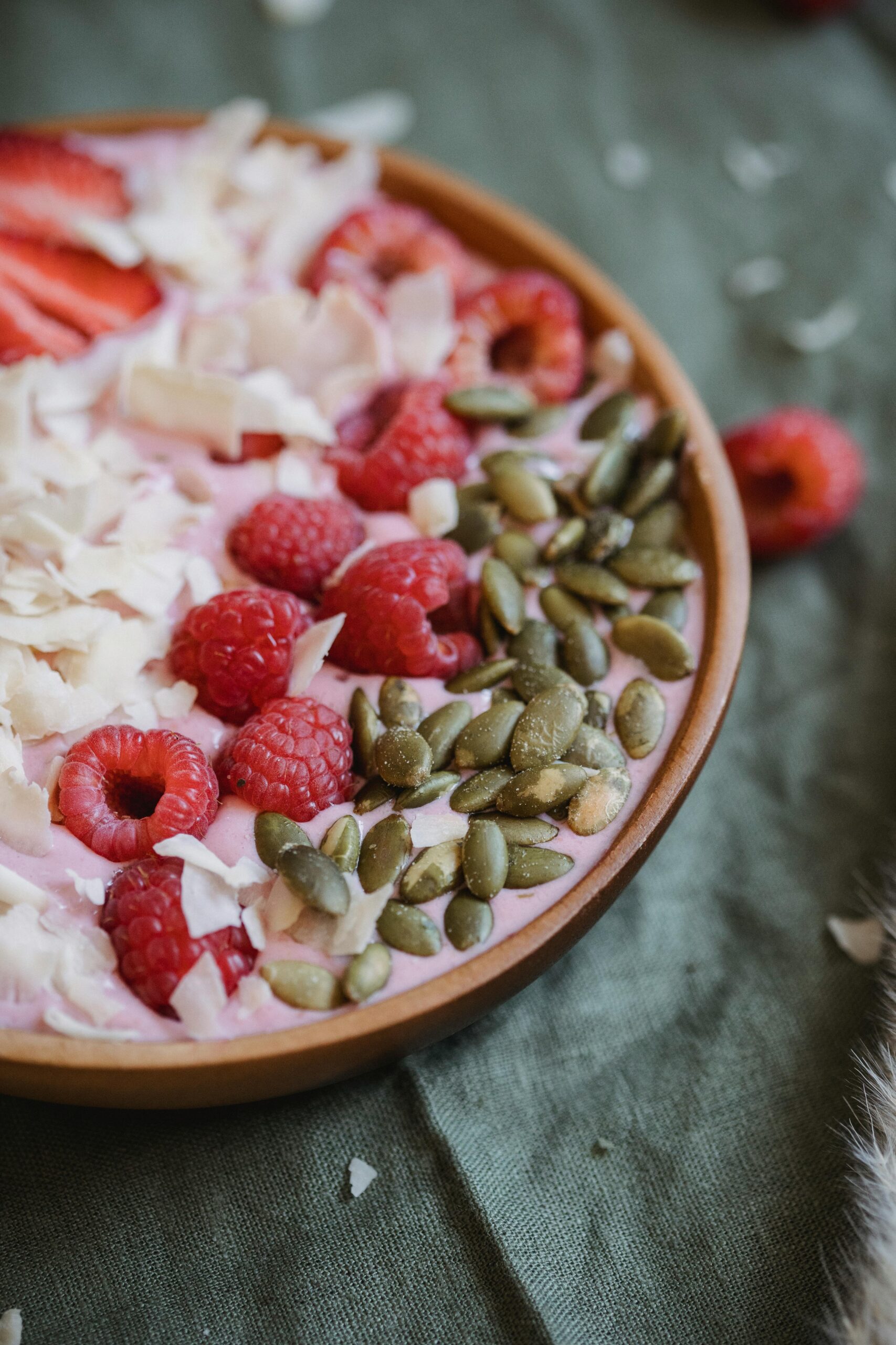 Vibrant smoothie bowl topped with fresh raspberries, pumpkin seeds, and coconut flakes.